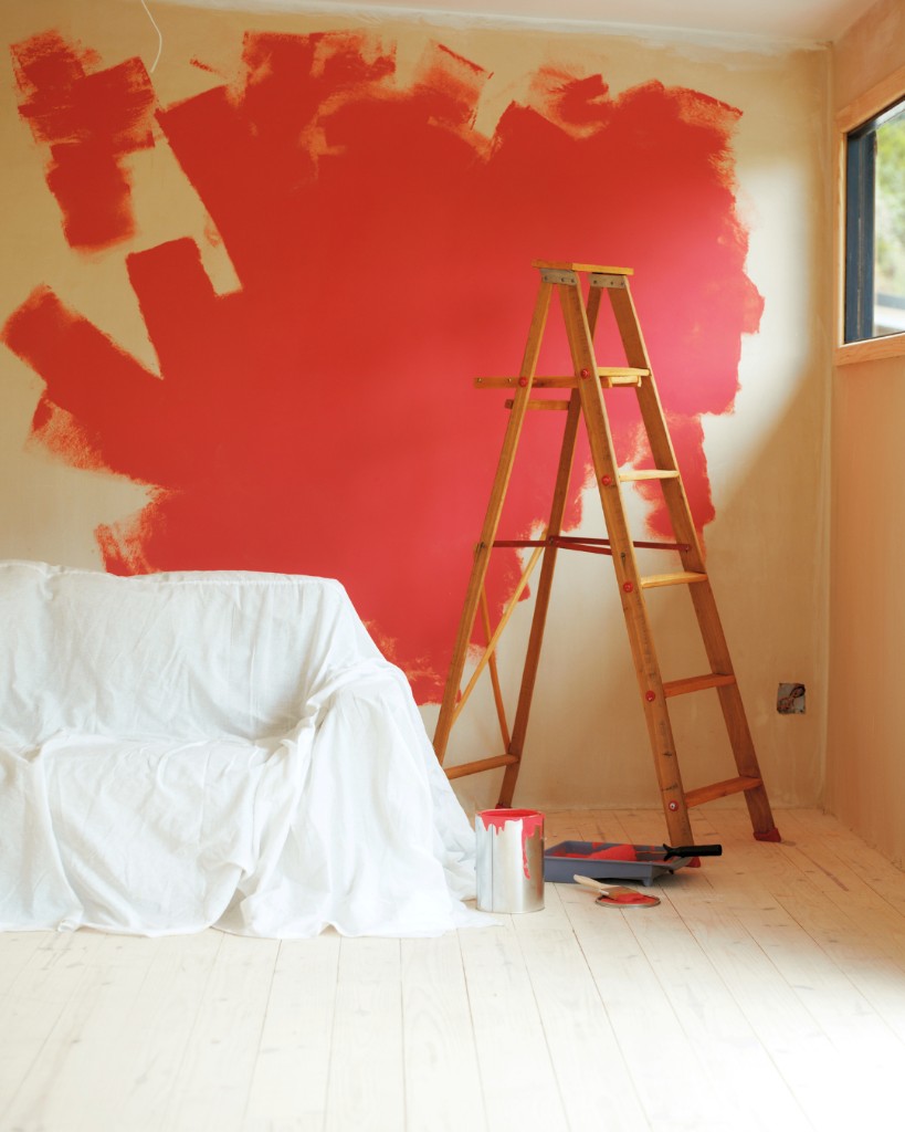 Decorating room in progress with red paint, ladder and covered furniture